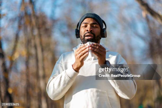 young man blowing his nose while exercising outdoors - allergie stockfoto's en -beelden