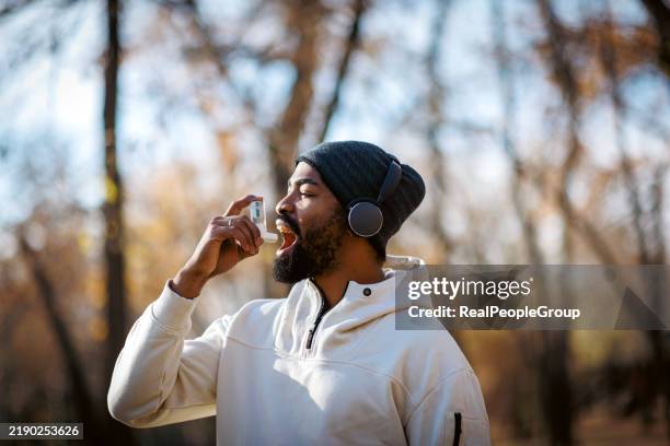 homem novo que usa o inalador da asma ao exercitar-se ao ar livre em um parque - inalador-de-alívio-para-asma - fotografias e filmes do acervo