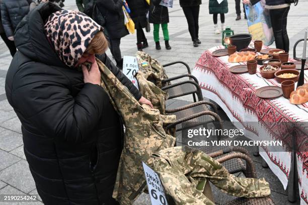 Woman kisses the uniform of her son, who has been in captivity for 680 days, as she stands next to a symbolic Christmas table set with traditional...