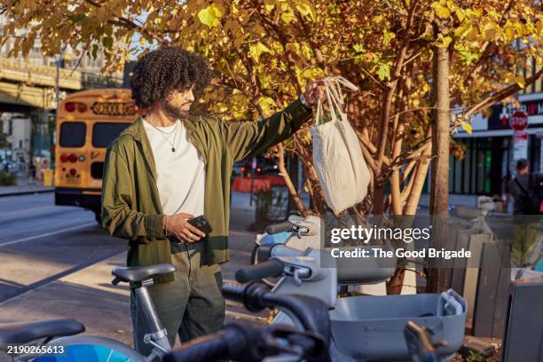 young man renting electric bicycle in city - bicycle sharing system stock pictures, royalty-free photos & images