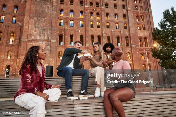 male and female friends sharing takeout food at city park - new york food stock pictures, royalty-free photos & images