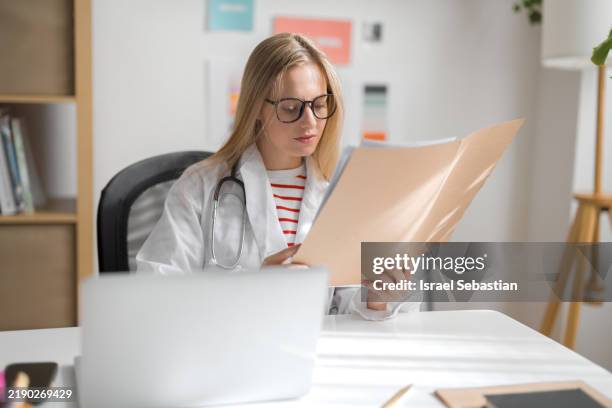 female doctor reading medical records in modern office - medizinische testergebnisse stock-fotos und bilder