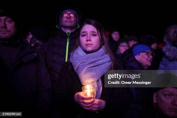 Woman holds a candle as others watch a prayer ceremony on large screens set outside the Magdeburg Dom church, the day after a terror attack that has...