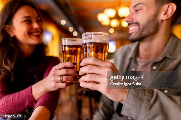 happy couple toasting with beer glasses in a pub - lager stock pictures, royalty-free photos & images