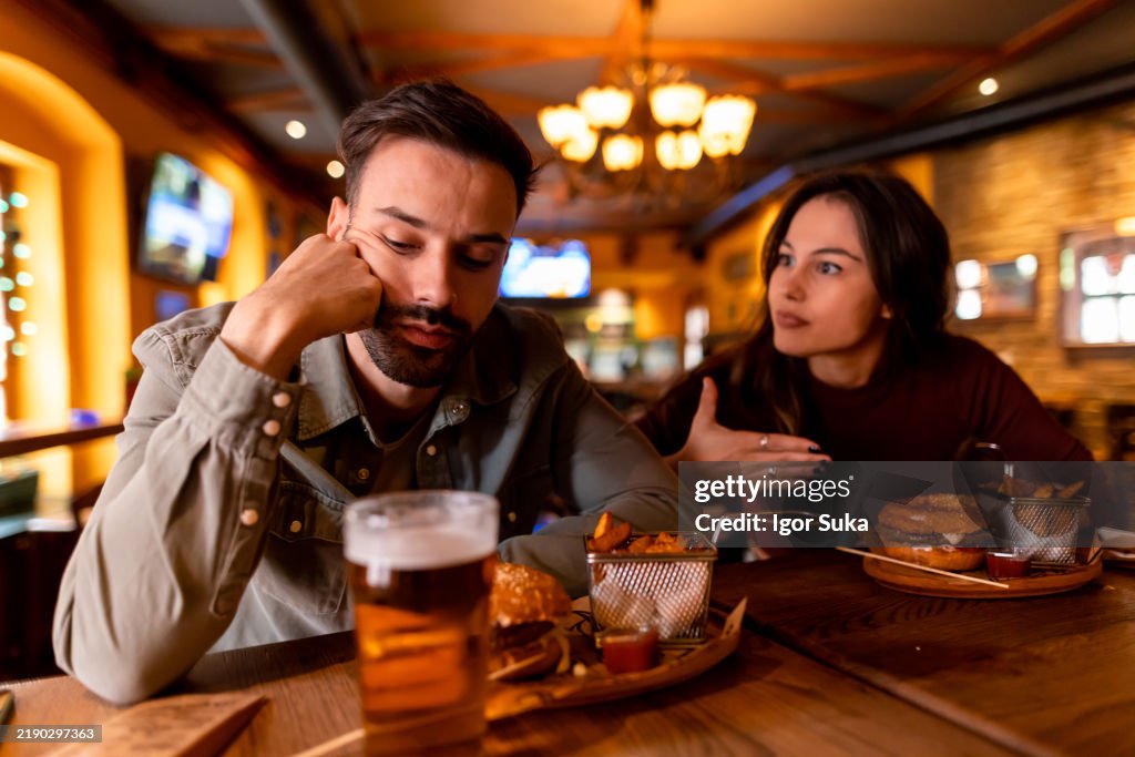 Young couple arguing at restaurant table with beer and burgers