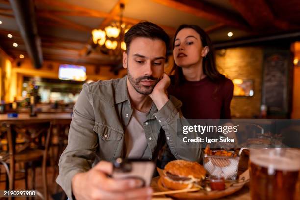 young man ignoring girlfriend while using smartphone in restaurant - envy stock pictures, royalty-free photos & images