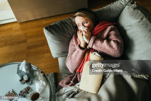 woman lying on a sofa while having a flu and feeling sick and sneezing. - pneumonia imagens e fotografias de stock