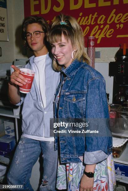 American actor Brad Pitt, wearing a light blue shirt over a white t-shirt, while holding a disposable Coca-Cola cup, and American singer Debbie...