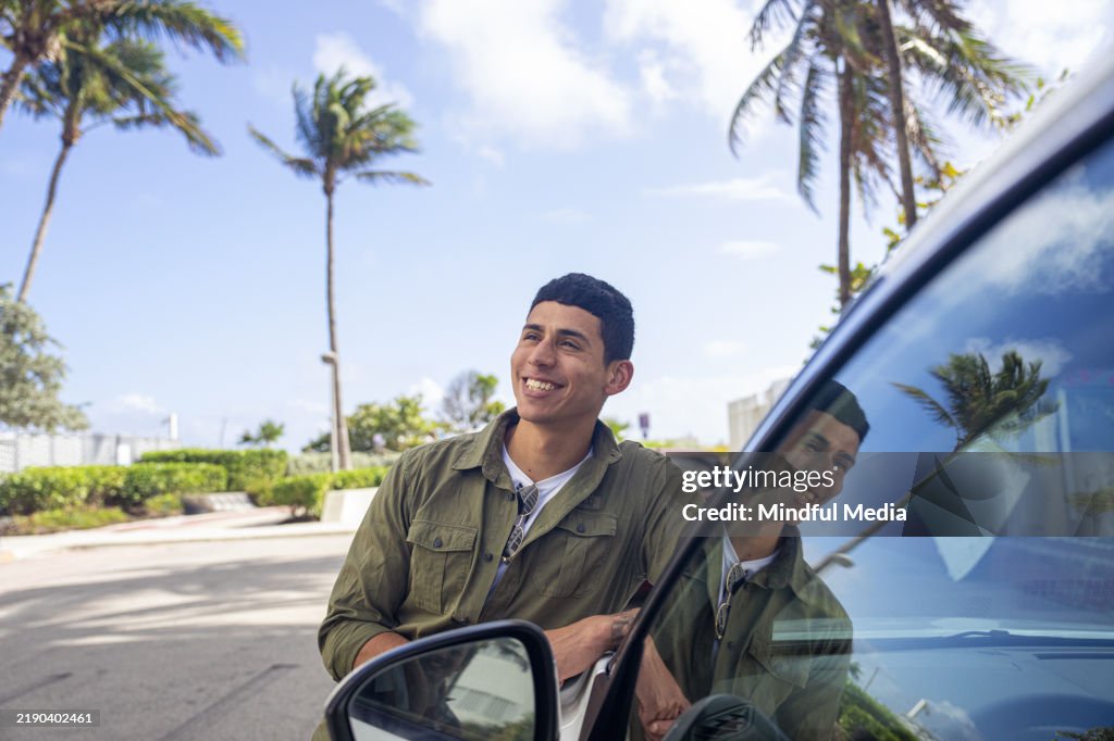 Junger Mann, der neben seinem gemieteten Auto steht, während er die Stadt Miami in Florida, USA, besucht