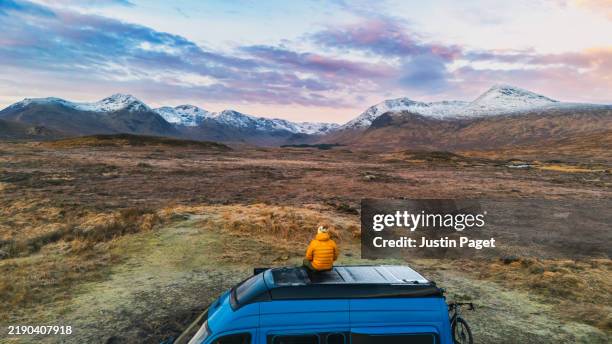 an elevated/drone view of a mature man sitting on the top of his campervan on a cold winter's morning - scottish highlands stock pictures, royalty-free photos & images