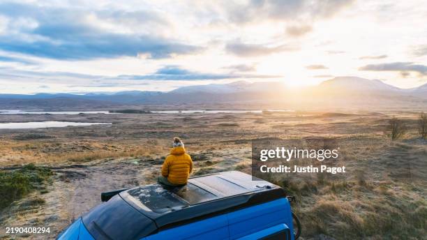 an elevated/drone view of a mature man sitting on the top of his campervan on a cold winter's morning - non urban scene stock pictures, royalty-free photos & images
