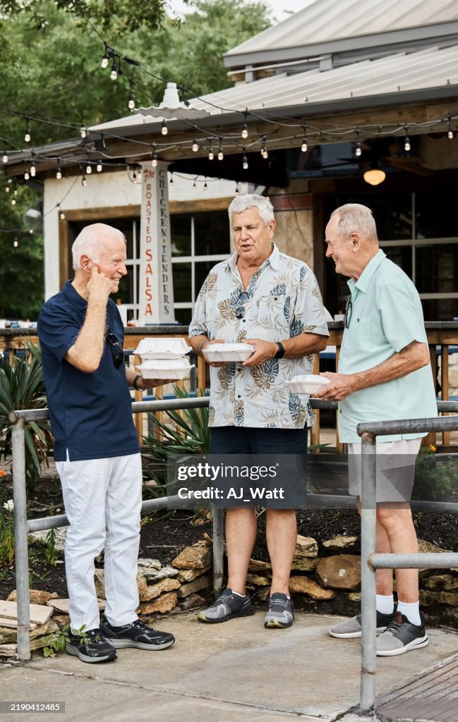 Senior friends holding to-go food standing out of restaurant