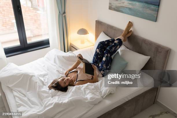 woman reading a book in her bedroom - woman legs up bed stock pictures, royalty-free photos & images