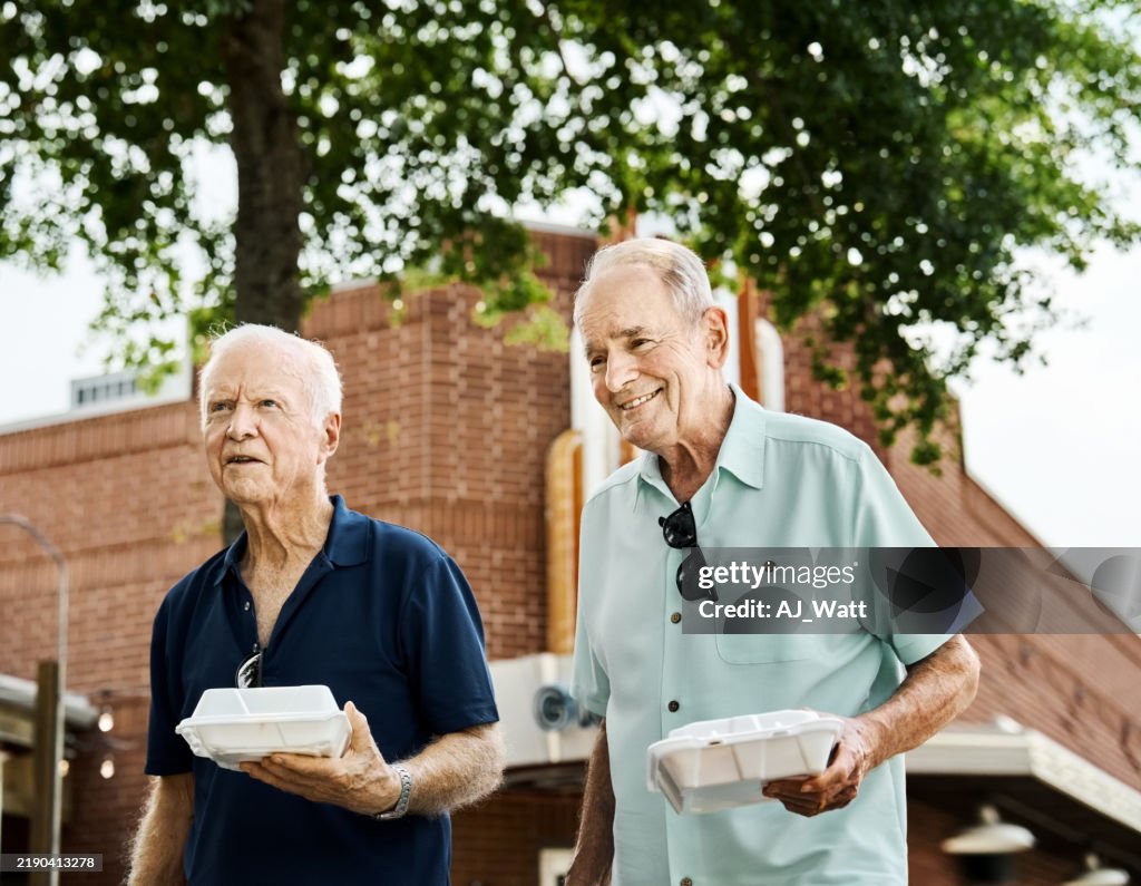 Two happy senior male friends with takeout food walking outdoors