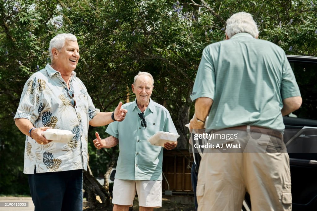 Group of senior men talking with takeout containers by parked car