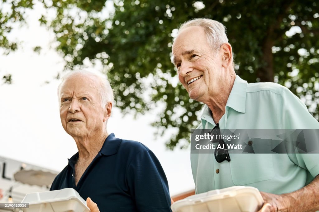 Two happy Senior men with to-go food boxes walking outdoors