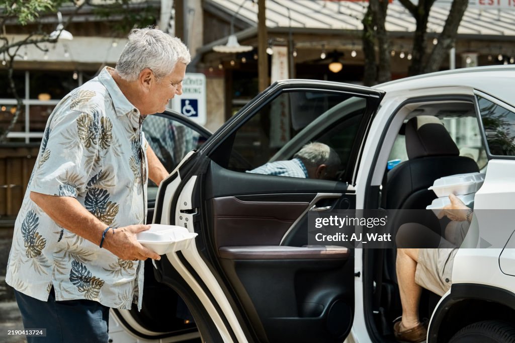 Senior man bidding farewell to friend leaving in car after lunch together
