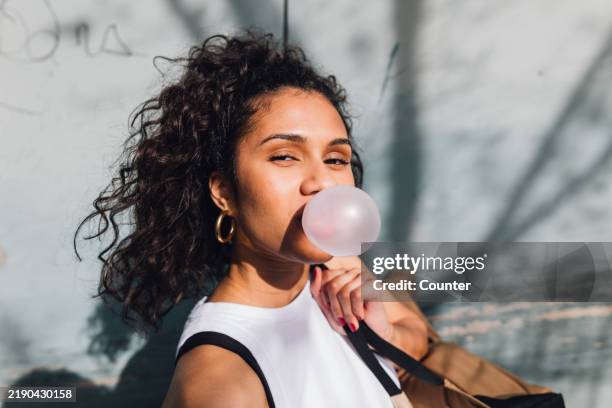 multiracial woman blowing bubble gum bubble in sun - kauwgom stockfoto's en -beelden