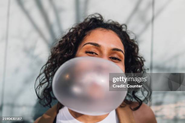 portrait of multiracial woman blowing bubble gum bubble in sun smiling - girl power stock pictures, royalty-free photos & images