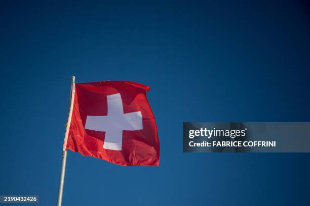 This photograph shows a Swiss flag waving in a blue sky in St.Moritz on December 21, 2024.