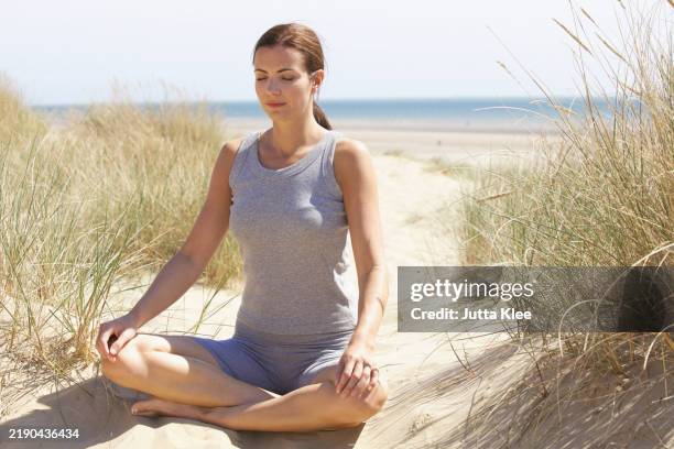 woman practicing yoga on sand dune by ocean - hand on knee stock pictures, royalty-free photos & images