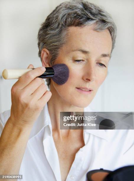 woman holding compact mirror applying blush - woman applying blush stock pictures, royalty-free photos & images
