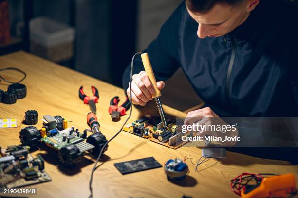 junger mann lötet elemente auf leiterplatte - lötkolben stock-fotos und bilder