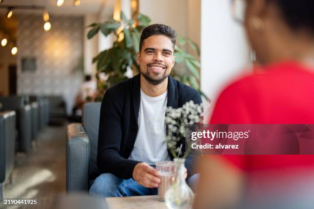 smiling young man in a cafe conversing over drinks - hot drink stock pictures, royalty-free photos & images