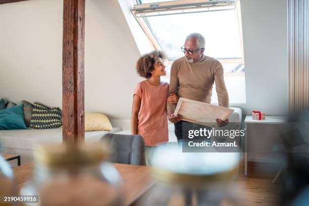 mature mixed race couple looking at painting in home interior - granddaughter stock pictures, royalty-free photos & images