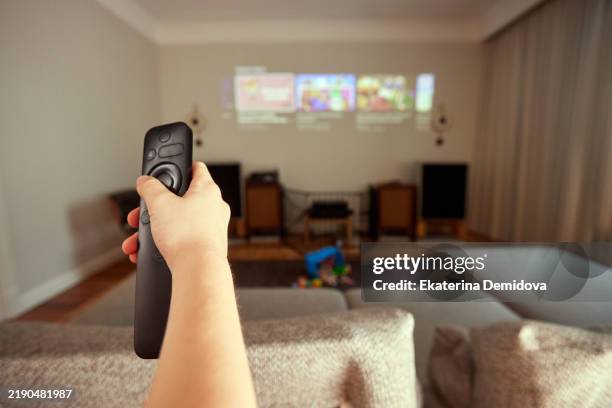 person on sofa holding remote control, pointing at streaming service menu projected on wall - subscription stock pictures, royalty-free photos & images