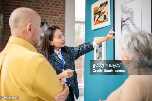 curator explaining artwork to visitors in an art gallery setting - espetáculo de arte imagens e fotografias de stock