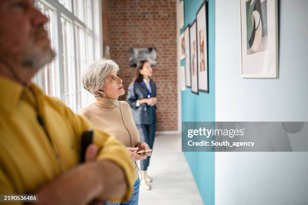 people viewing artwork in a gallery under guidance of a curator - espetáculo de arte imagens e fotografias de stock