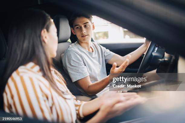 young man getting driving lessons from mother while sitting in car - learning to drive stock pictures, royalty-free photos & images