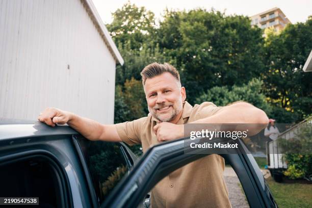 portrait of smiling mature man leaning on car door in back yard - car door stock pictures, royalty-free photos & images