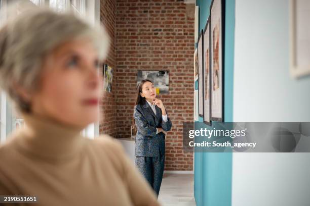 art gallery visitors observing displayed works with a curator present. - art show stock pictures, royalty-free photos & images