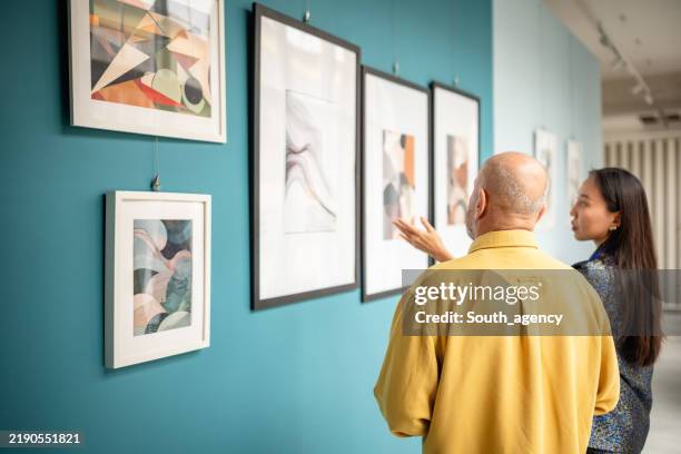 two people discussing artworks in a contemporary art gallery exhibit - espetáculo de arte imagens e fotografias de stock