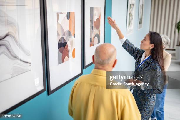 art gallery curator presenting artwork to visitors in a contemporary setting - espetáculo de arte imagens e fotografias de stock