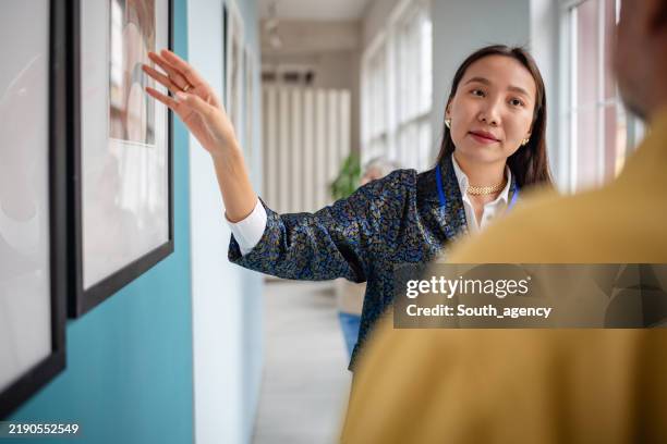 art curator discussing framed pictures in a modern gallery exhibit setting - espetáculo de arte imagens e fotografias de stock