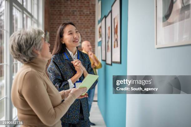 kunstkurator, der galeriebesucher einbindet, während er über ausgestellte kunstwerke diskutiert - museumswärter stock-fotos und bilder