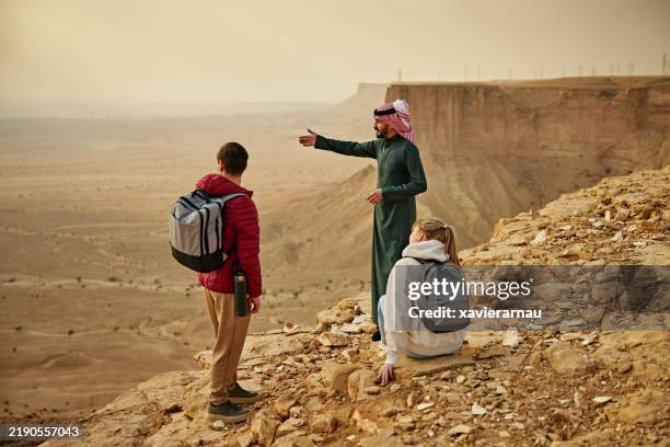saudi guide showing desert landscape to young couple at edge of the world - saudi arabian culture stock pictures, royalty-free photos & images