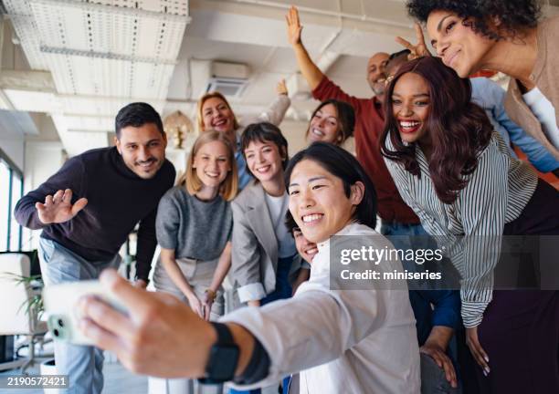 team taking group selfie during relaxed office gathering in modern workspace - organised group photo stock pictures, royalty-free photos & images