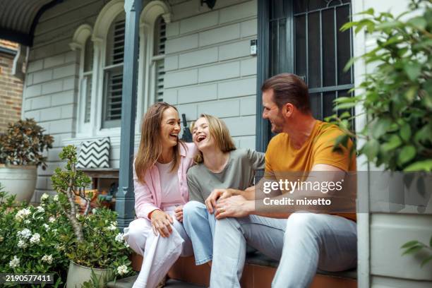 mother father and daughter sharing laughter while sitting on front of their house - porch stock pictures, royalty-free photos & images
