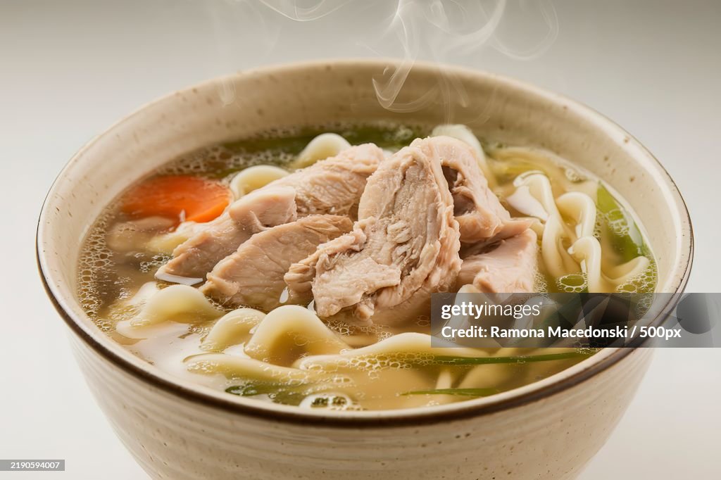 A bowl of chicken noodle soup on a white background