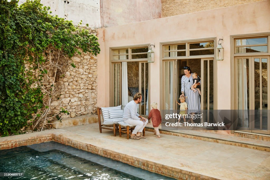 Wide shot family relaxing on poolside patio of villa during vacation