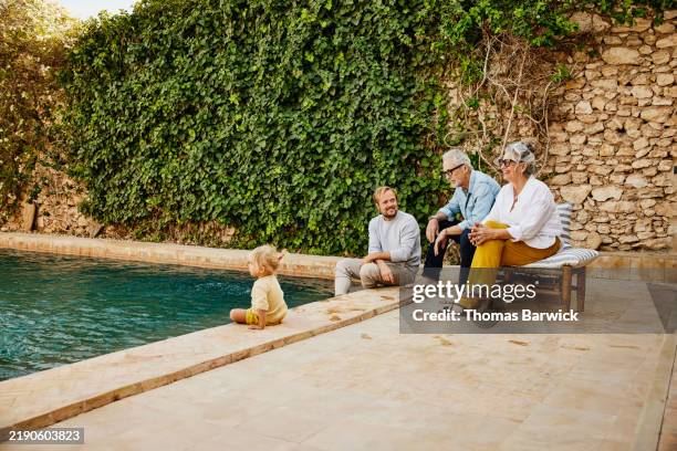 wide shot smiling multigenerational family relaxing at tropical villa - richesse photos et images de collection