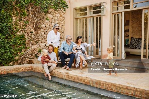 wide shot smiling multigenerational family relaxing at tropical villa - richesse photos et images de collection