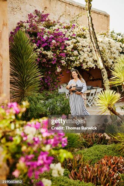 wide shot mother walking in garden with sleeping toddler son in arms - buganville foto e immagini stock