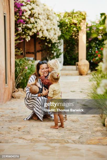 wide shot son kissing mother on cheek in garden of tropical villa - buganville foto e immagini stock