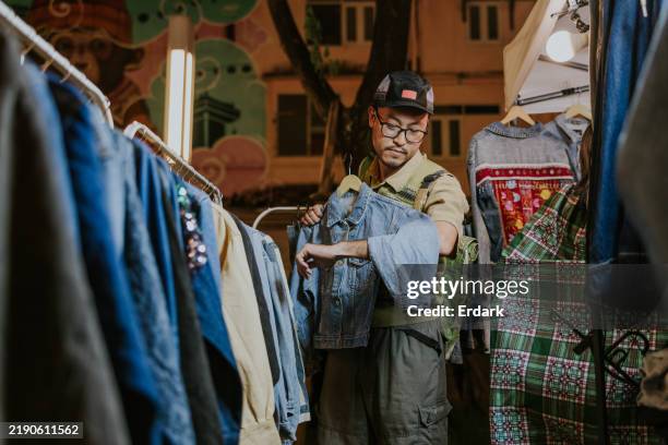 marché de jeans de 2ème main, l’homme touriste asiatique est intéressant dans une veste. - industrie de la mode photos et images de collection