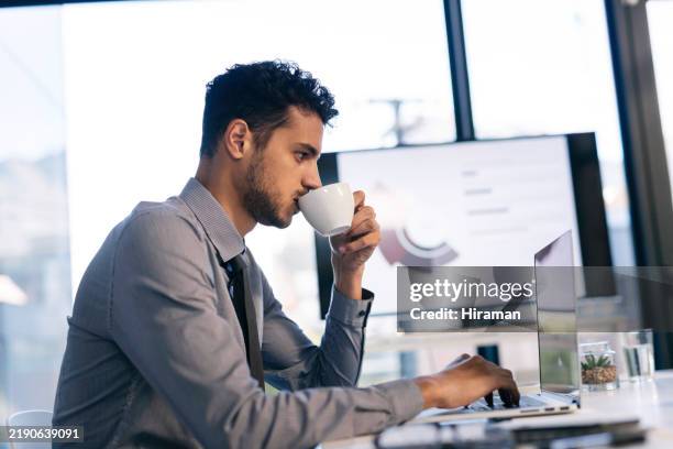young professional working on laptop while enjoying coffee in modern office environment - hierarquia de corporação imagens e fotografias de stock